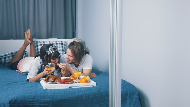 Happy Newlywed Couple Enjoying Breakfast In Bed. Man Giving Stawberry To His Girlfriend. Slow Motion. High Quality Photo