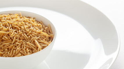 Indian spicy snacks (Namkeen) - Bikaneri Besan Bhujia in a white bowl, made with chickpea flour (Besan), side view, against the white background.