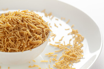 Indian spicy snacks (Namkeen) - Bikaneri Besan Bhujia in a white bowl, made with chickpea flour (Besan), side view, against the white background.