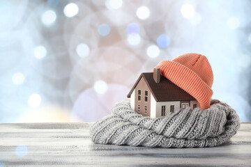 Figure of house and warm clothes on table against blurred lights. Concept of heating season