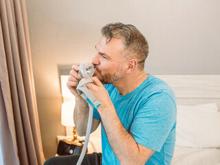 Mature happy man with chronic breathing issues considers using sitting on the bed in bedroom with...