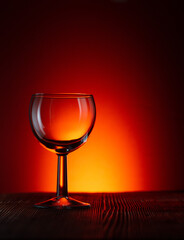 Silhouette of an empty glass wine or rum glass on a dark illuminated red background