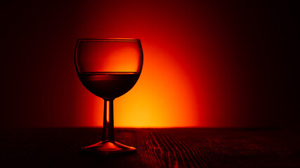 Silhouette of a glass wine or rum glass on a dark illuminated red background