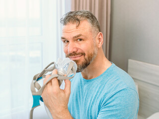 Mature happy man with chronic breathing issues considers using sitting on the bed in bedroom with...