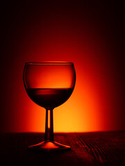 Silhouette of a glass wine or rum glass on a dark illuminated red background