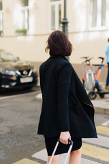 Beautiful woman in black dress on a background of an urban landscape with a suitcase