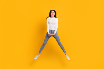 Fototapeta na wymiar Full size photo of optimistic cute girl jump wear sweater jeans sneakers isolated on yellow color background