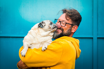 My best friend dog concept with funny scene adult man with beard and pug dog kissing him on the face - people and animals have fun and love together in friendship - Powered by Adobe