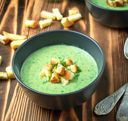 Creamy spinach soup with crackers, herbs and chia seeds. Green soup on a wooden table. Side view, close-up.