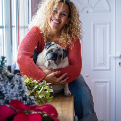 Cheerful dog owner beautiful adult female at home hugging her pug with love and tenderly - concept...