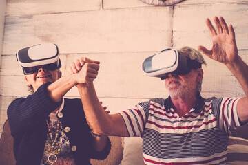 Youthful concept with old senior couple enojying goggled headset together in online modern games and virtual reality experience - happy elderlu lifestyle for man and woman at home
