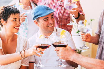 Group of cheerful caucasian friends enjoy and celebrate together clinking with red wine and cocktails glasses - people celebrate and enjoy friendship with smile and fun in daylight