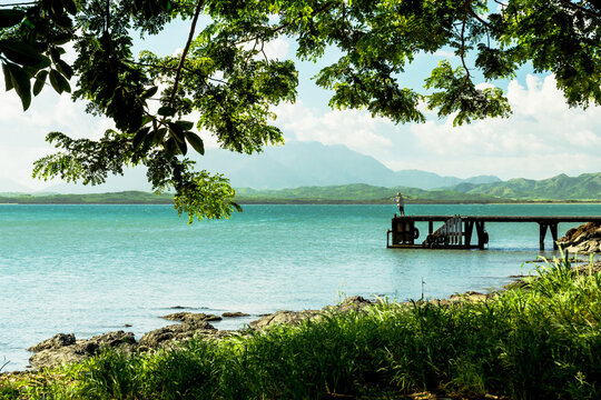 Seaside view with a wooden wharf and a fisherman and mountains on the background near Voh village, Chasseloup bay, New Caledonia.