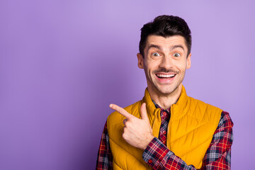 Photo of cute excited young man wear yellow sleeveless jacket pointing one finger empty space...