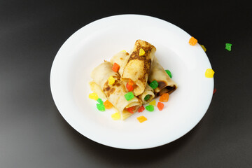 Thin pancakes stuffed with candied fruits. pancakes lie in a white plate on a black