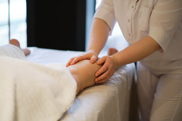 Obraz premium Detail of hands massaging human calf muscle.Therapist applying pressure on female leg. Hands of massage therapist massaging legs of young woman in spa salon. Body care in spa salon for young woman.
