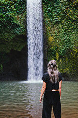 Young travelling woman standing in front of a pretty and large waterfall in the jungle of bali, indonesia.