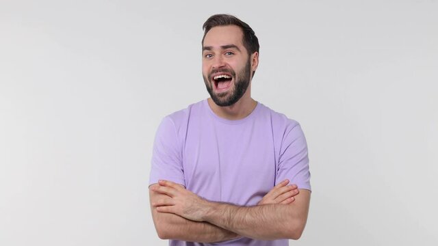 Funny laughing bearded young man 20s years old in pastel casual violet t-shirt isolated on white color wall background studio. People lifestyle concept. Holding hands crossed looking aside blinking
