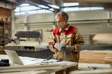 Carpenter with face mask using laptop and working on touchpad in a workshop.