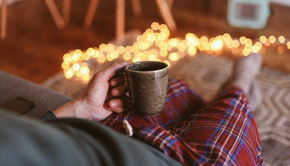 Man in check pyjamas sitting on a couch with a cup of tea