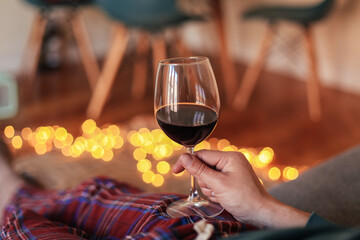 Man in check pyjamas holding a glass of red wine, cosy living room with candid light