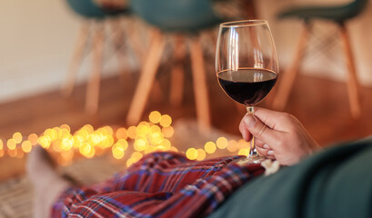 Man in check pyjamas holding a glass of red wine, cosy living room with candid light