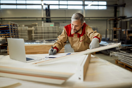 Mid adult worker taking notes while checking measurements at carpentry workshop.