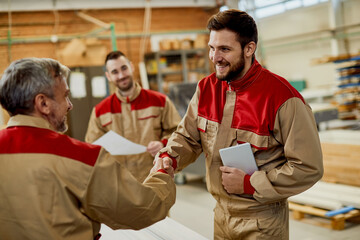 Happy carpenter handshaking with is colleague while greeting in a workshop.