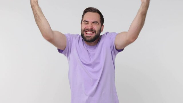 Happy joyful bearded young man 20s years old in casual pastel violet t-shirt isolated on white background studio. People lifestyle concept. Doing winner gesture celebrating clenching fists say yes