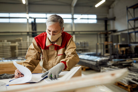 Male worker checking data while making furniture at carpentry workshop during coronavirus pandemic. - Powered by Adobe