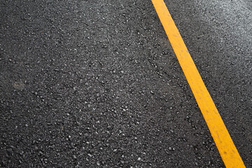 Close up black asphalt road surface texture with a yellow line.