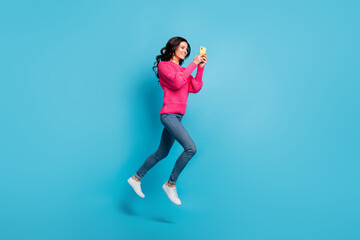 Full body profile side photo of happy brunette wavy haired girl hold phone go copyspace jump isolated on blue color background