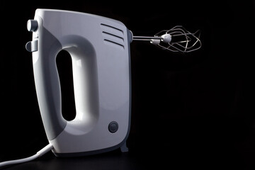 An electric hand mixer for beating eggs with stirring whisks on black surface.
