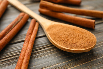 Cinnamon sticks and spoon with powder on wooden background