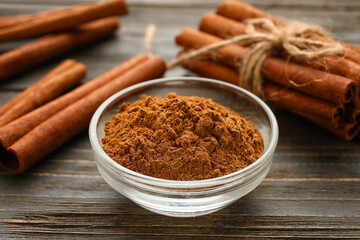 Cinnamon sticks and bowl with powder on wooden background