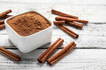 Cinnamon sticks and bowl with powder on wooden background
