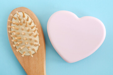 Heart shaped pink bar of soap and wooden hair brush on a light blue background. Top view, copy space.