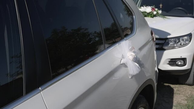 Two white expensive cars stand near the house and are decorated with bouquets of flowers and bows from fatin and in one opens a luggage carrier