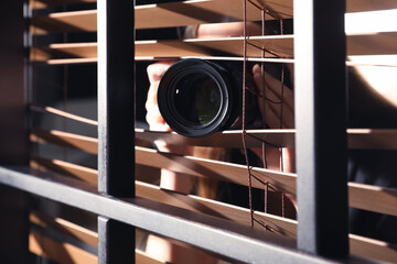 Private detective with camera spying near window indoors, closeup - obrazy, fototapety, plakaty