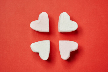 Fototapeta premium in the center of the red background, four white and light pink marshmallows in the form of a heart