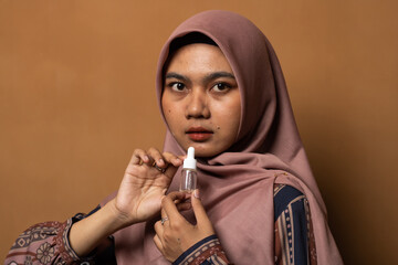 Asian young woman showing skincare products on gold background.