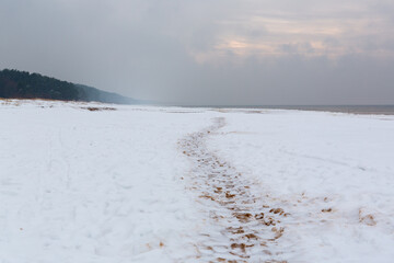 Calm winter seaside scene with footprints in snow at the Baltic sea on a cloudy day in January in Saulkrasti in Latvia