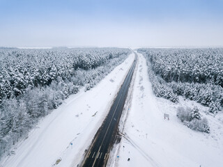 Drone view of a paved road in a snowy winter forest. Winter road conditions