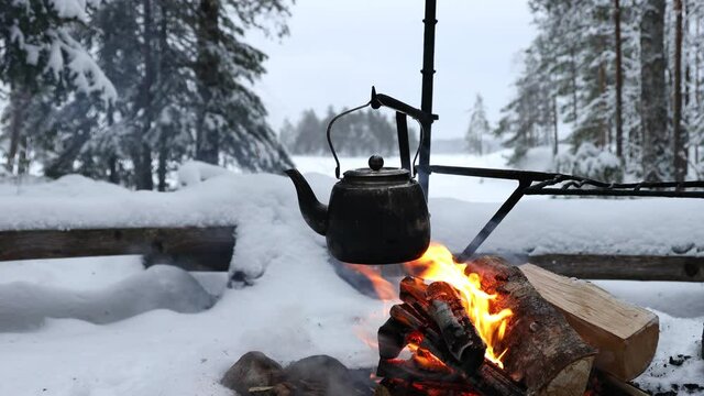 Coffee pot hanging over the fire outside in the winter forest. Winter theme. Camping, hiking concept. 