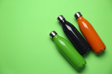 Different thermo bottles on green background, flat lay. Space for text