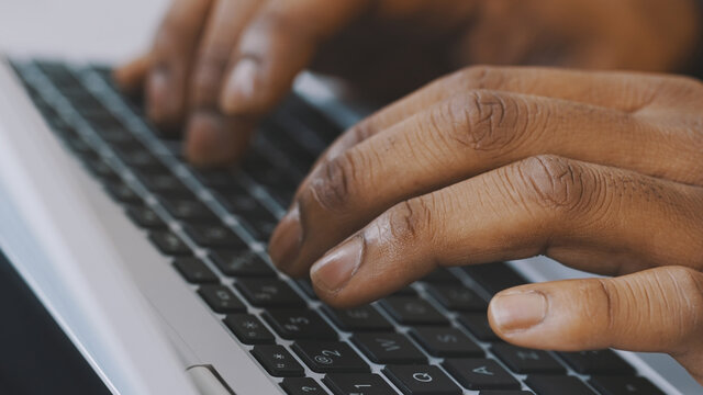 Close up shot of hands of unrecognizable afro-american businessman typing on laptop keyboard. High quality photo