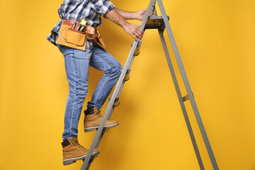 Professional builder climbing up metal ladder on yellow background, closeup - Powered by Adobe