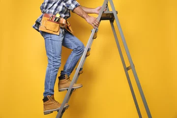Deurstickers Professional builder climbing up metal ladder on yellow background, closeup © New Africa