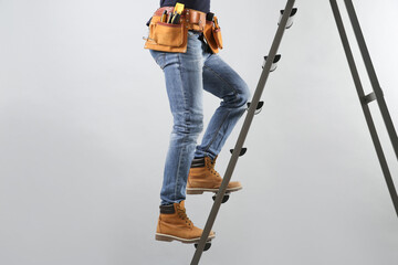 Professional builder climbing up metal ladder on grey background, closeup of legs - obrazy, fototapety, plakaty