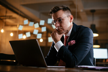 Naklejka na ściany i meble Young businessman using laptop in his office. Handsome man working at his workplace..